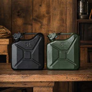 Zwarte en groene metalen jerrycan van 5 liter naast elkaar op een houten tafel tegen een donkere houten achtergrond.
